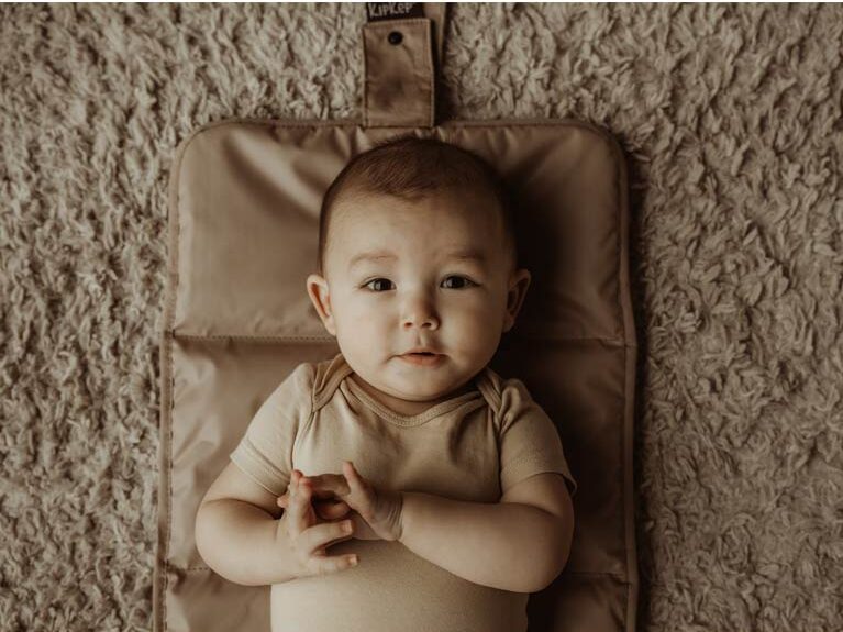 Baby lying on KipKep brown portable changing mat, soft and comfortable surface
