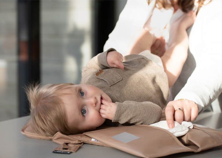 Baby lying on travel changing mat while parent prepares wipes for diaper change