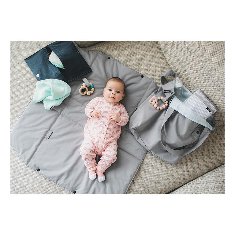 Baby on grey changing mat with diaper bag and accessories